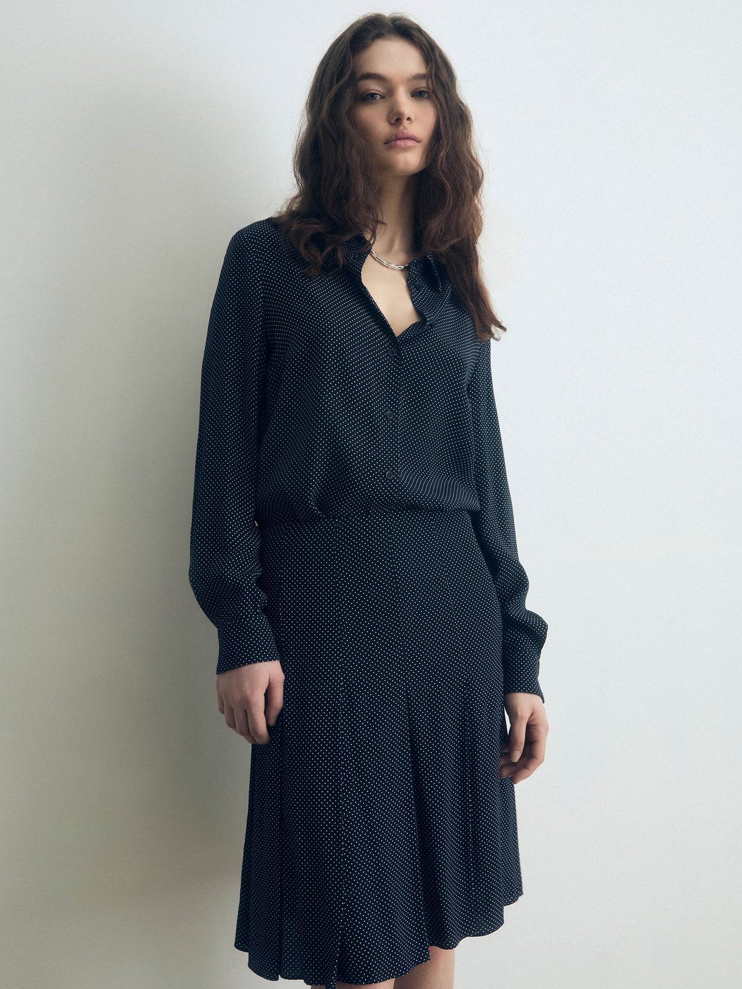 Model wearing a navy blouse with a subtle off-white micro-dot pattern, featuring a relaxed fit, long sleeves, and a soft drape, paired with a matching A-line skirt in the same dotted fabric.