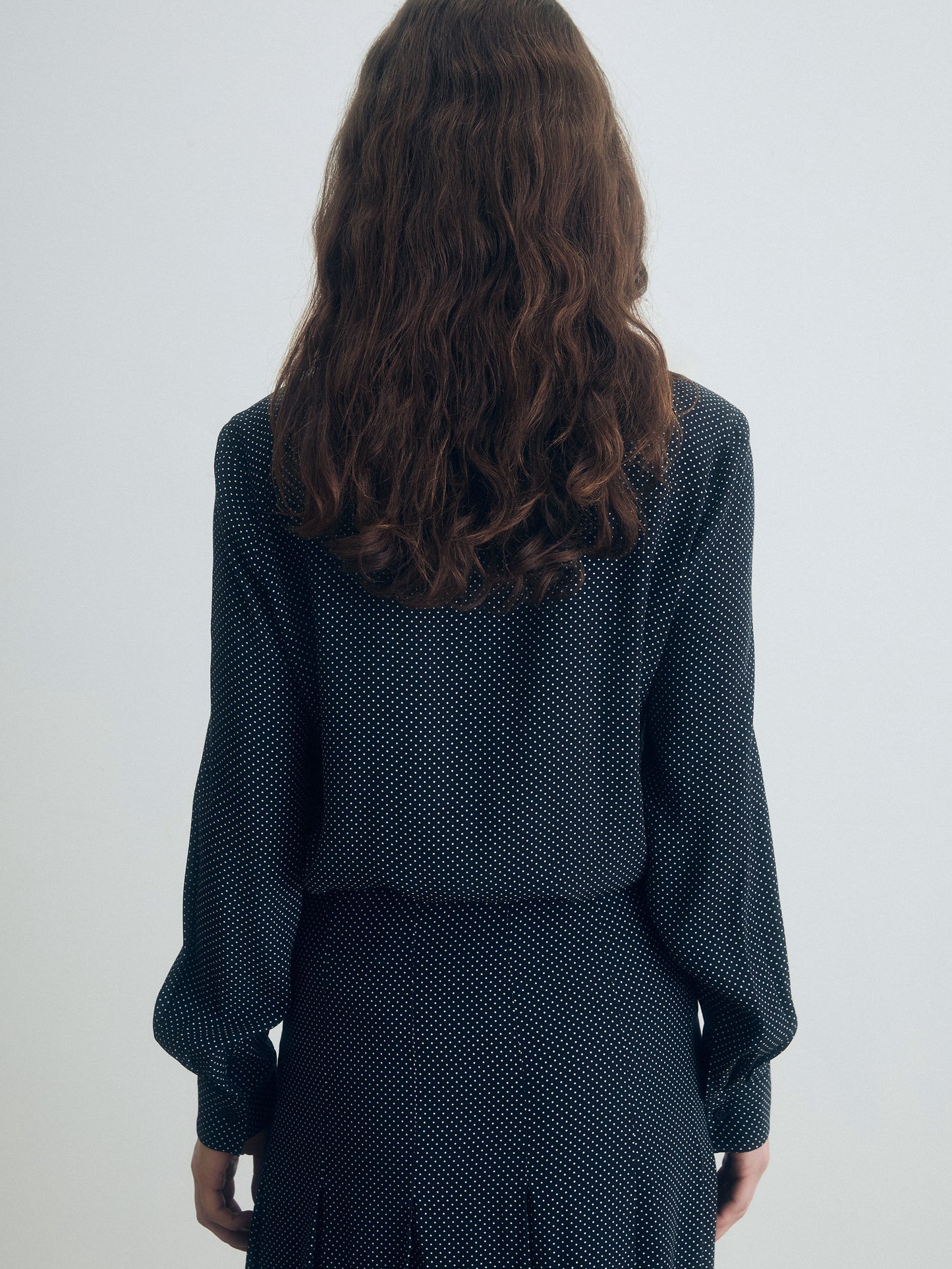 Person wearing a dark polka dot outfit against a white background
