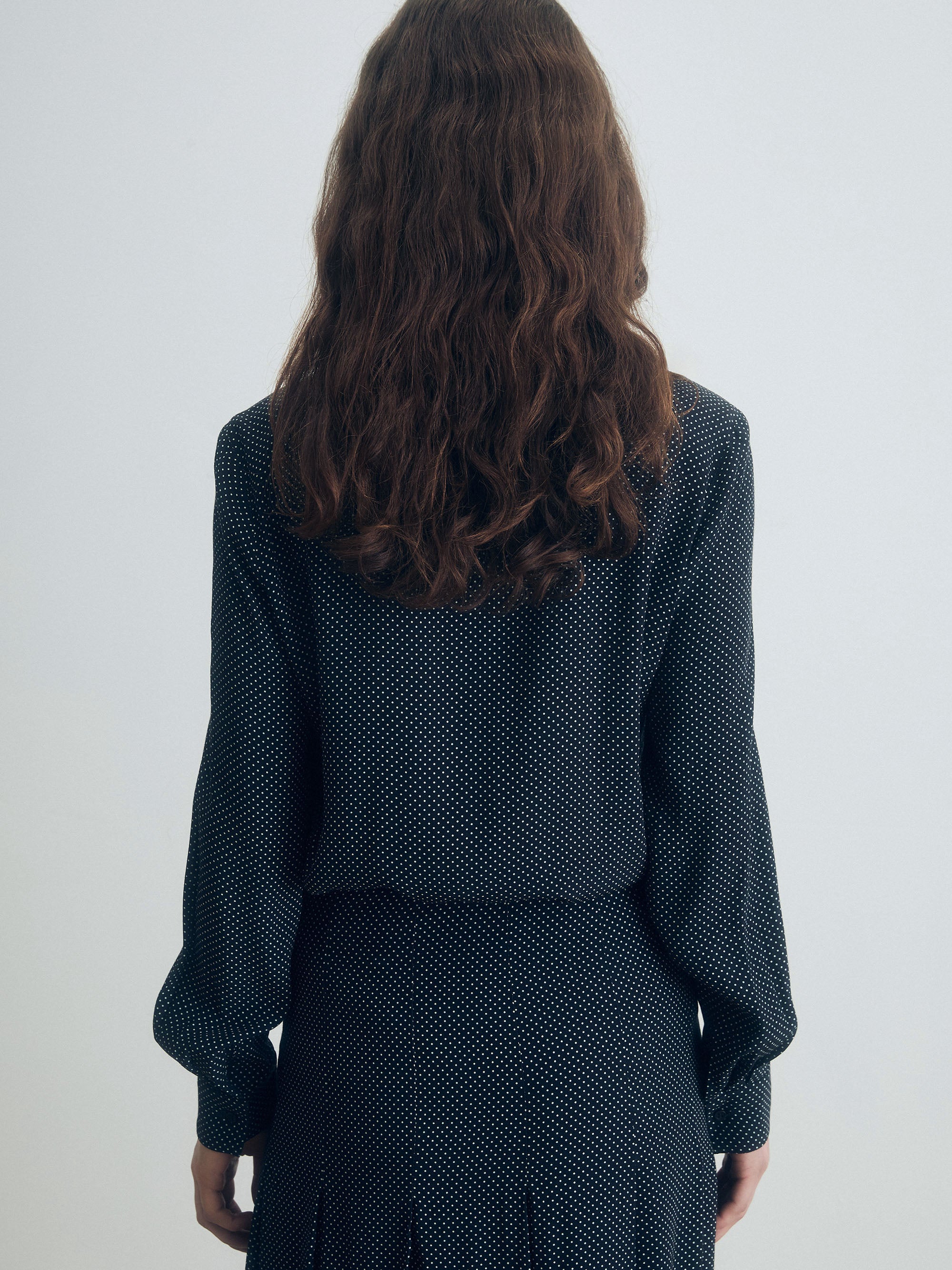 Person wearing a dark polka dot outfit against a white background