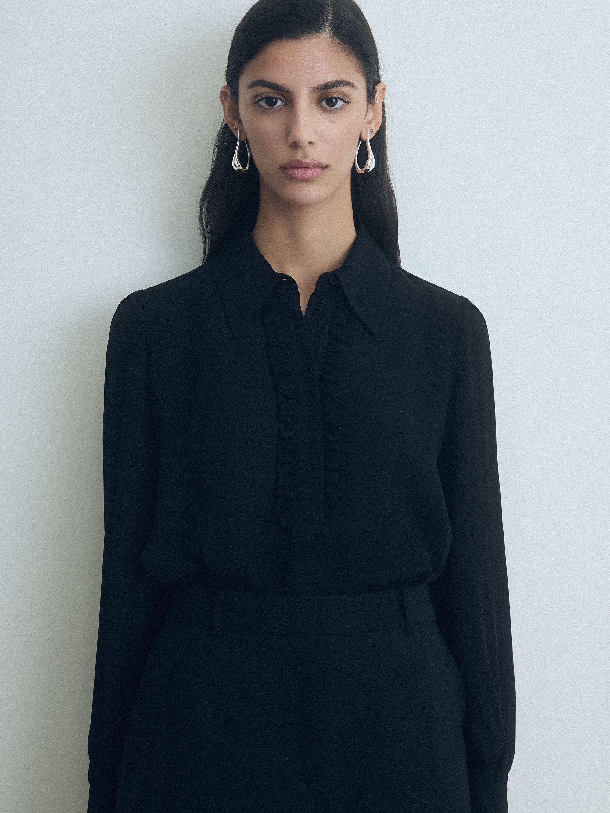 Woman wearing a black judith and charles blouse against a plain background