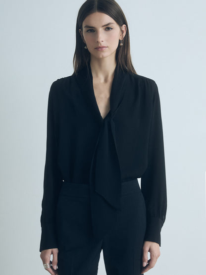 Woman wearing a black blouse with a tie against a light gray background