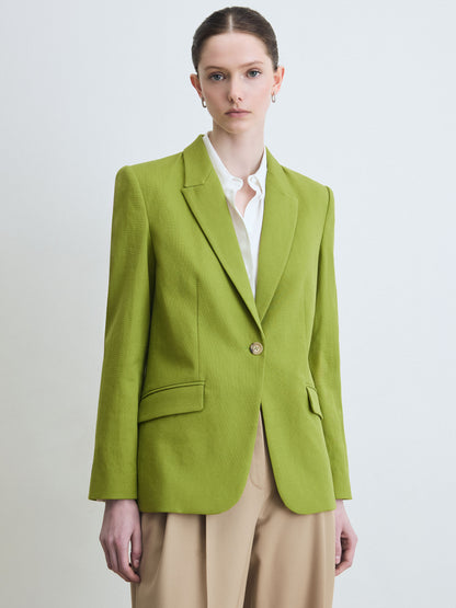 Woman wearing a green blazer over a white shirt on a light gray background