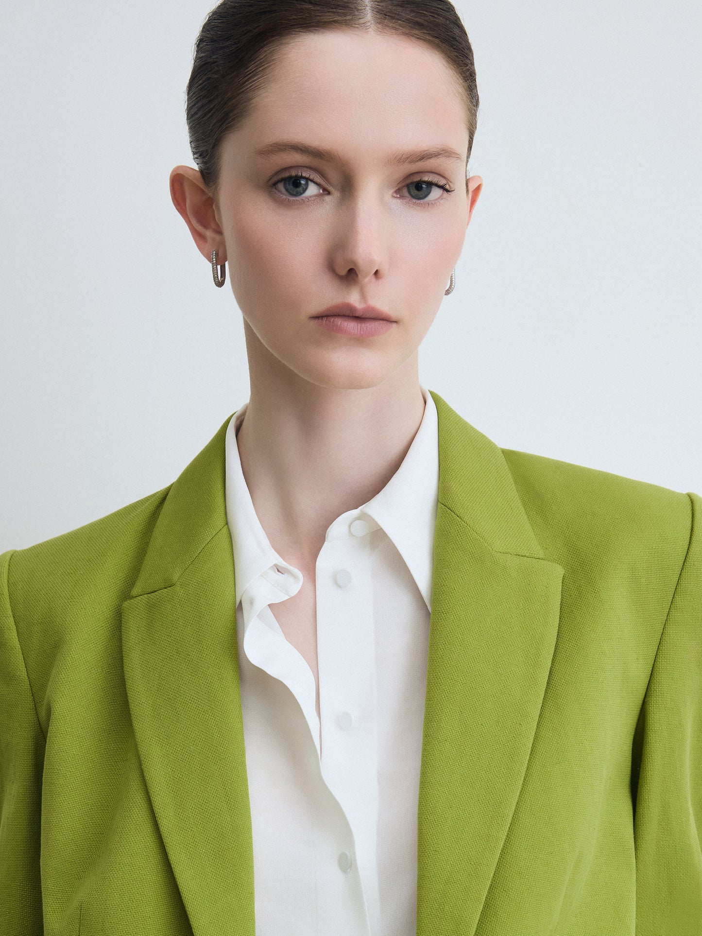 Woman wearing a green blazer over a white shirt on a light gray background