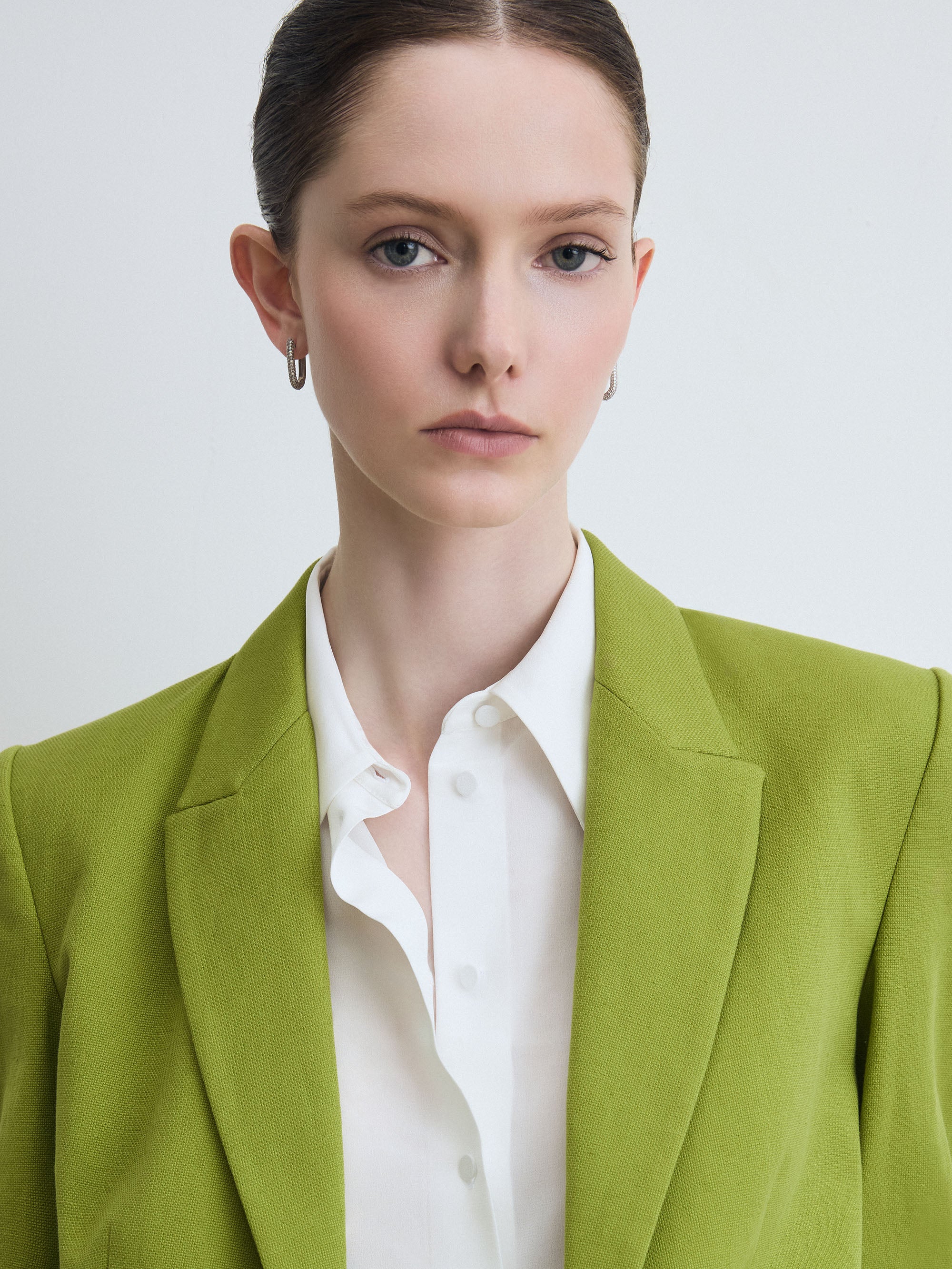 Woman wearing a green blazer over a white shirt on a light gray background