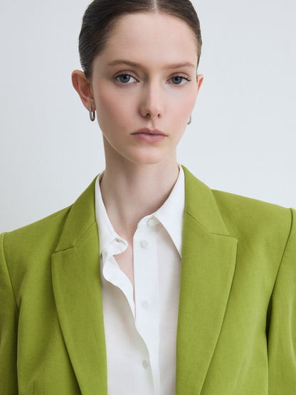 Woman wearing a green blazer over a white shirt on a light gray background
