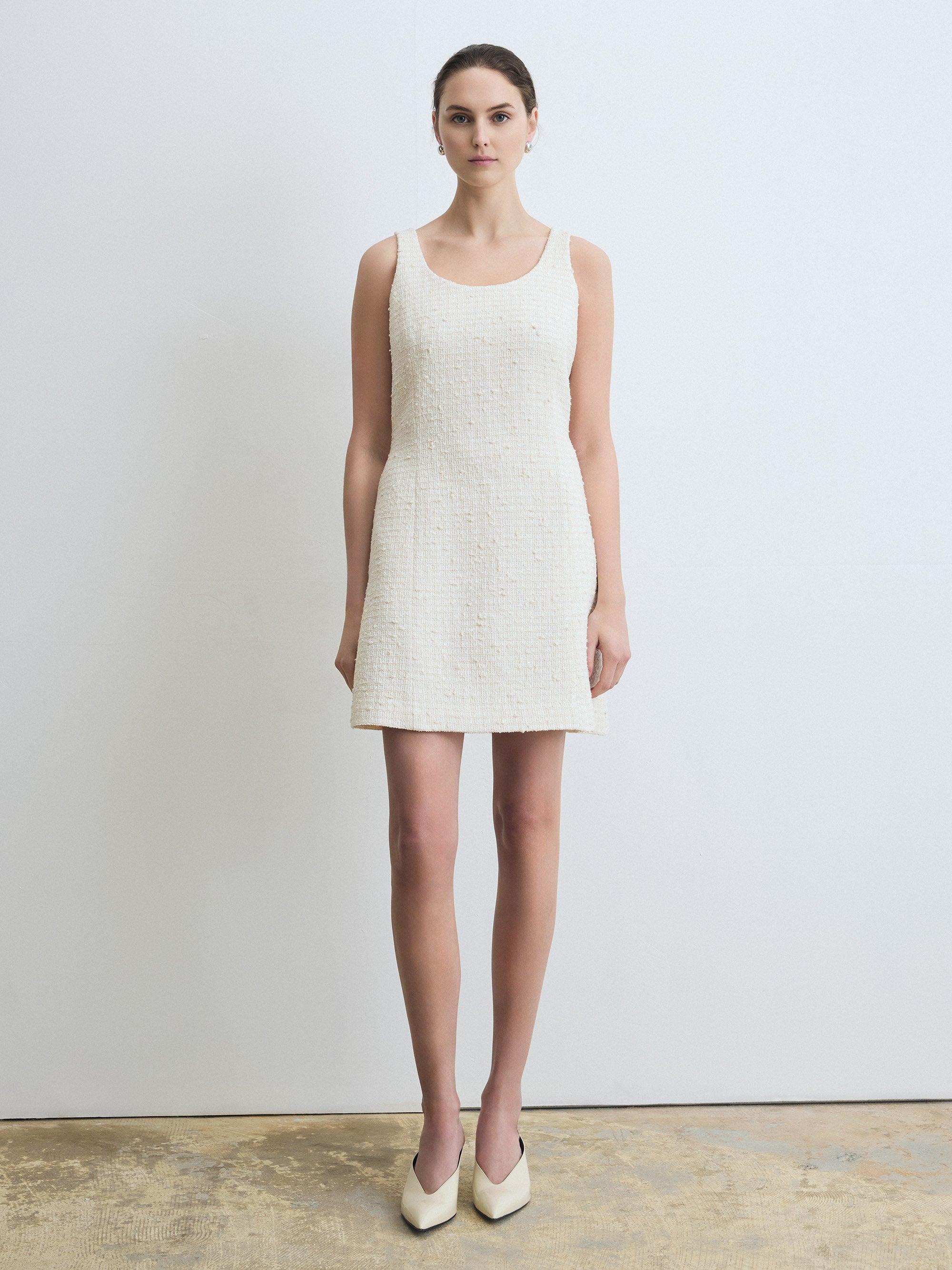 Woman wearing a cream sleeveless dress against a plain background