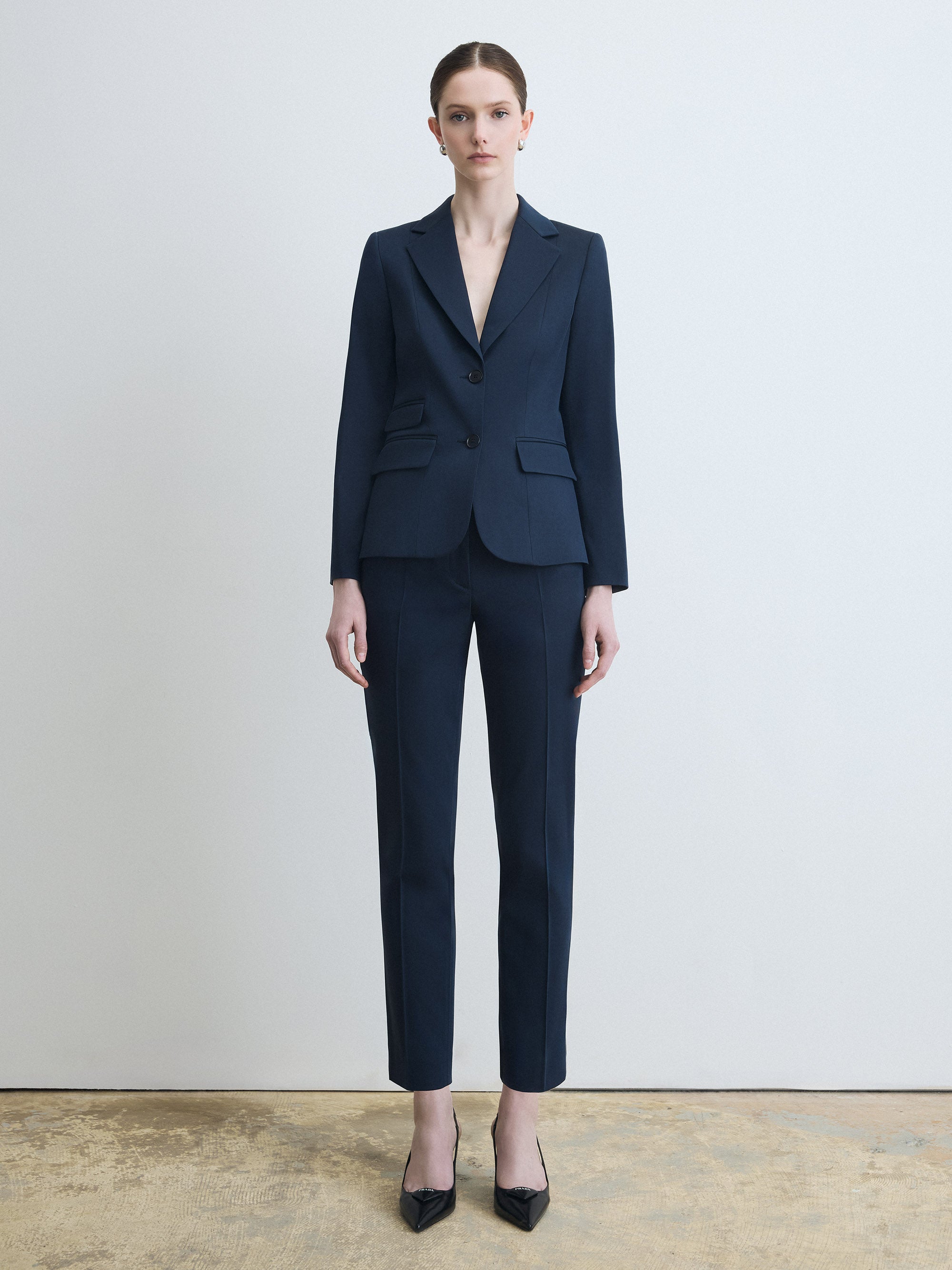Person wearing a navy blue suit standing against a plain background