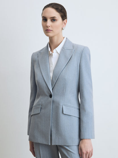 Woman wearing a light blue suit with a white shirt on a plain background