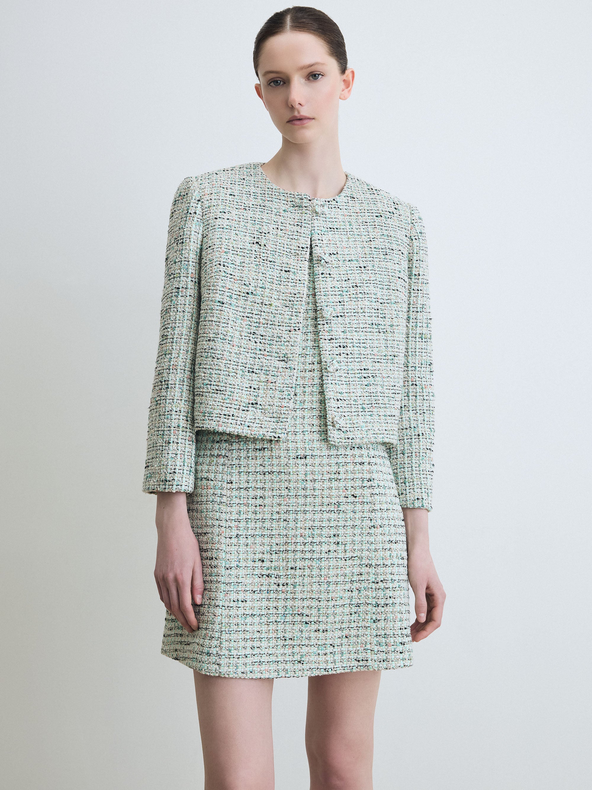 Woman wearing a mint tweed suit on a plain background