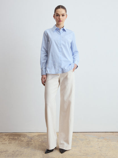 Person wearing a light blue striped shirt and beige pants against a plain background