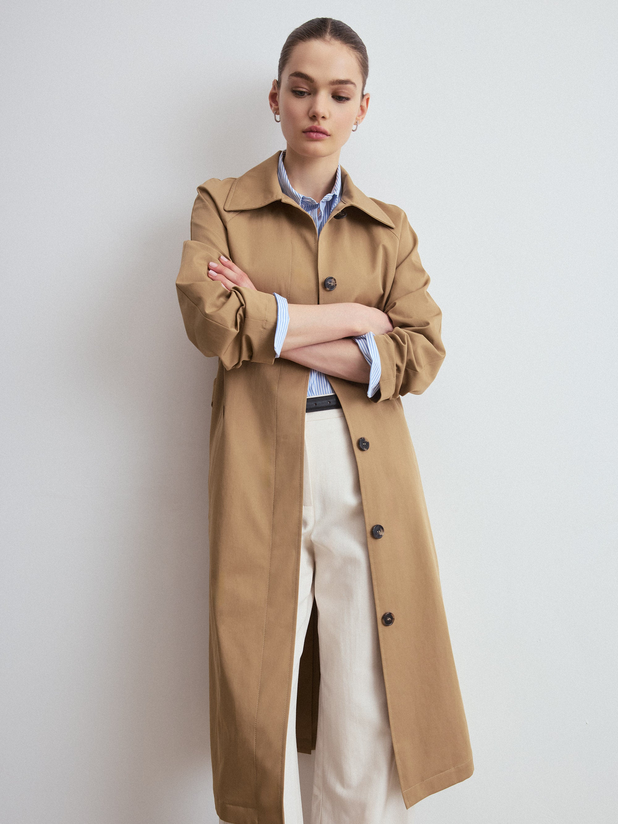 Woman wearing a camel trench coat against a plain background
