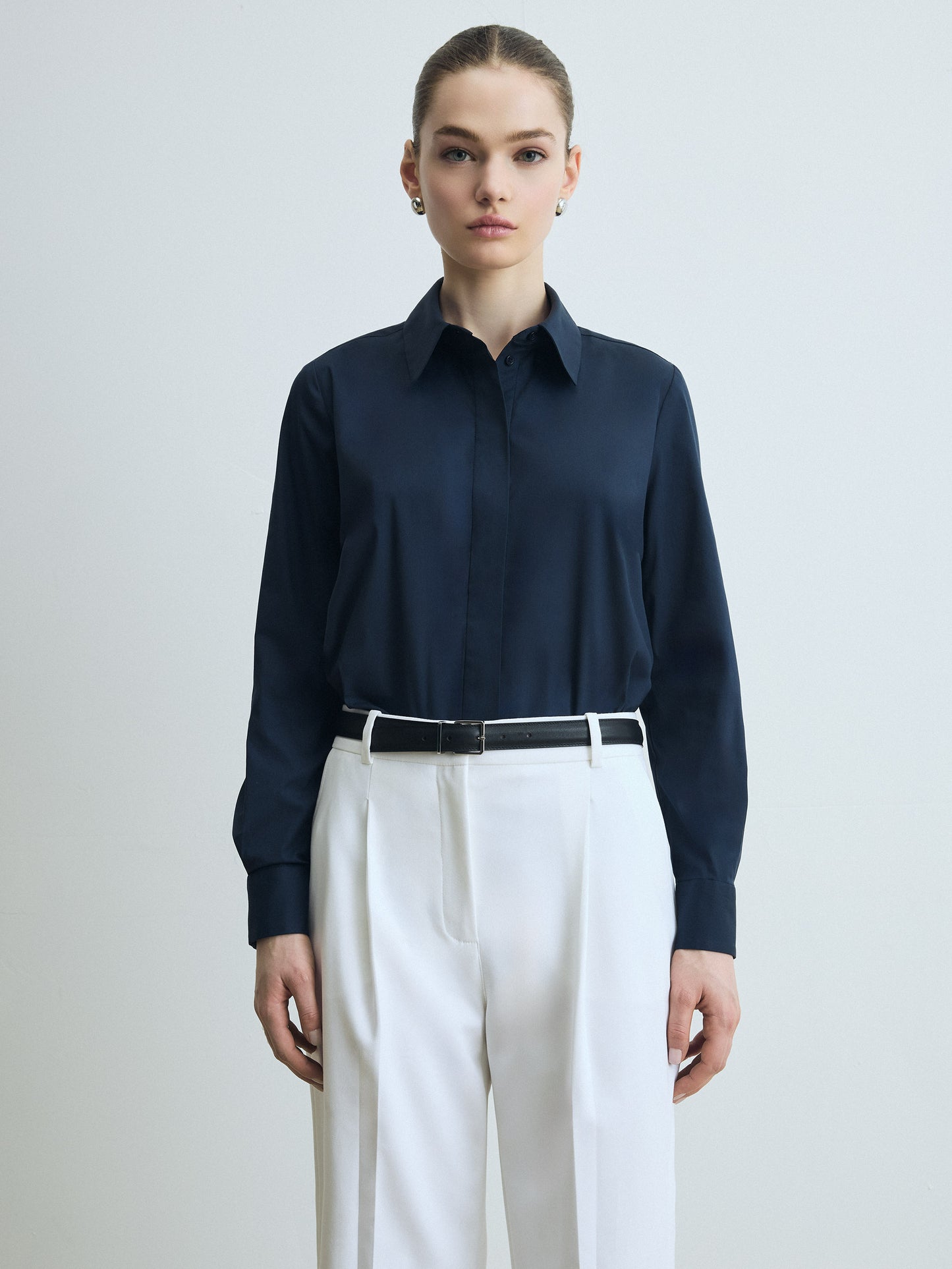 Person wearing a navy shirt and white pants on a plain background