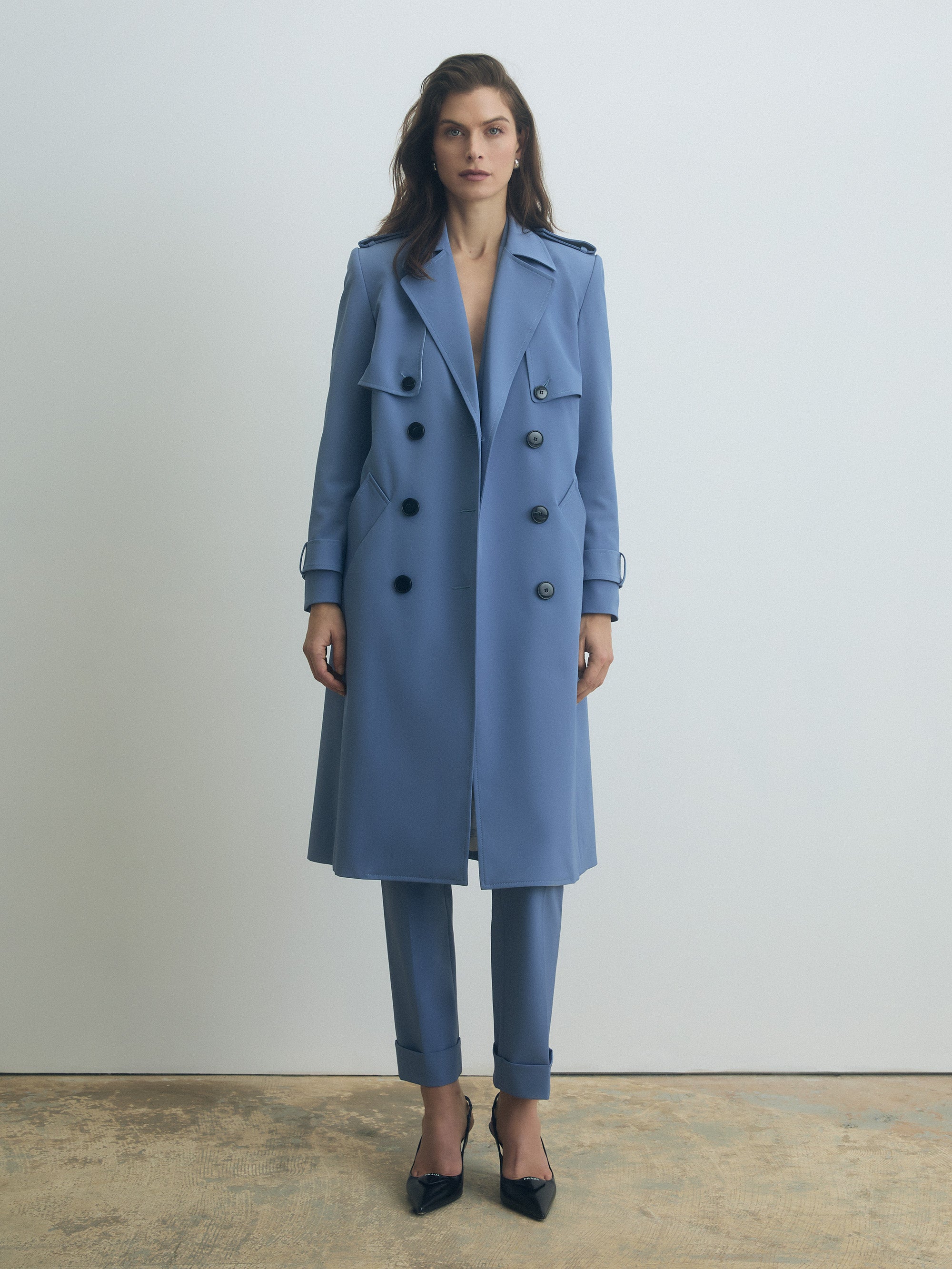Woman wearing a blue trench coat and pants on a plain background
