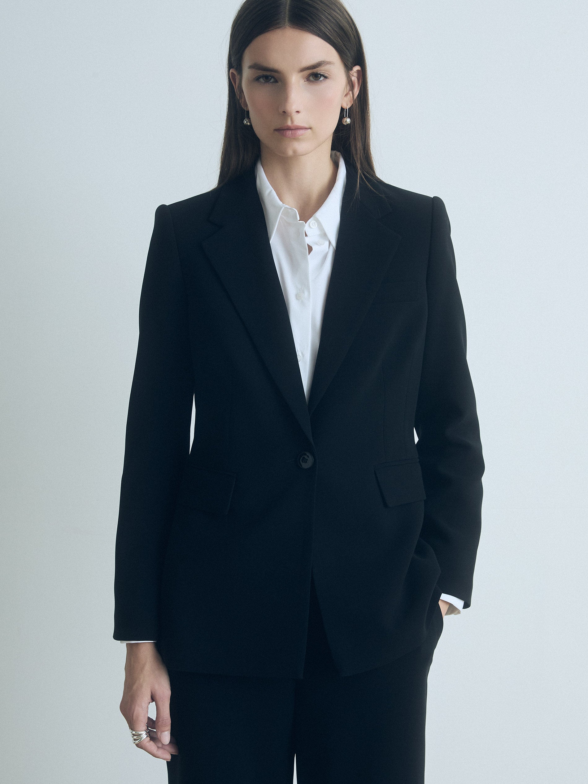 Model wearing a black jacket from Judith and Charles and white shirt on a light gray background