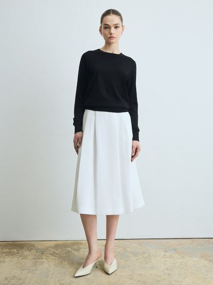 Woman wearing a black sweater and white skirt against a plain background