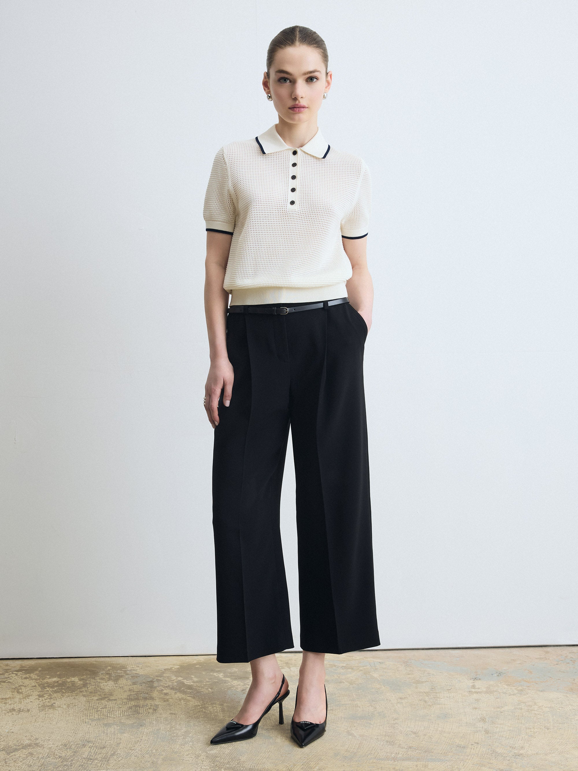 Woman wearing a white polo shirt with black trim and black wide-leg pants against a plain background