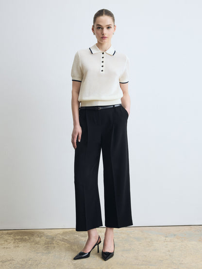 Woman wearing a white polo shirt with black trim and black wide-leg pants against a plain background