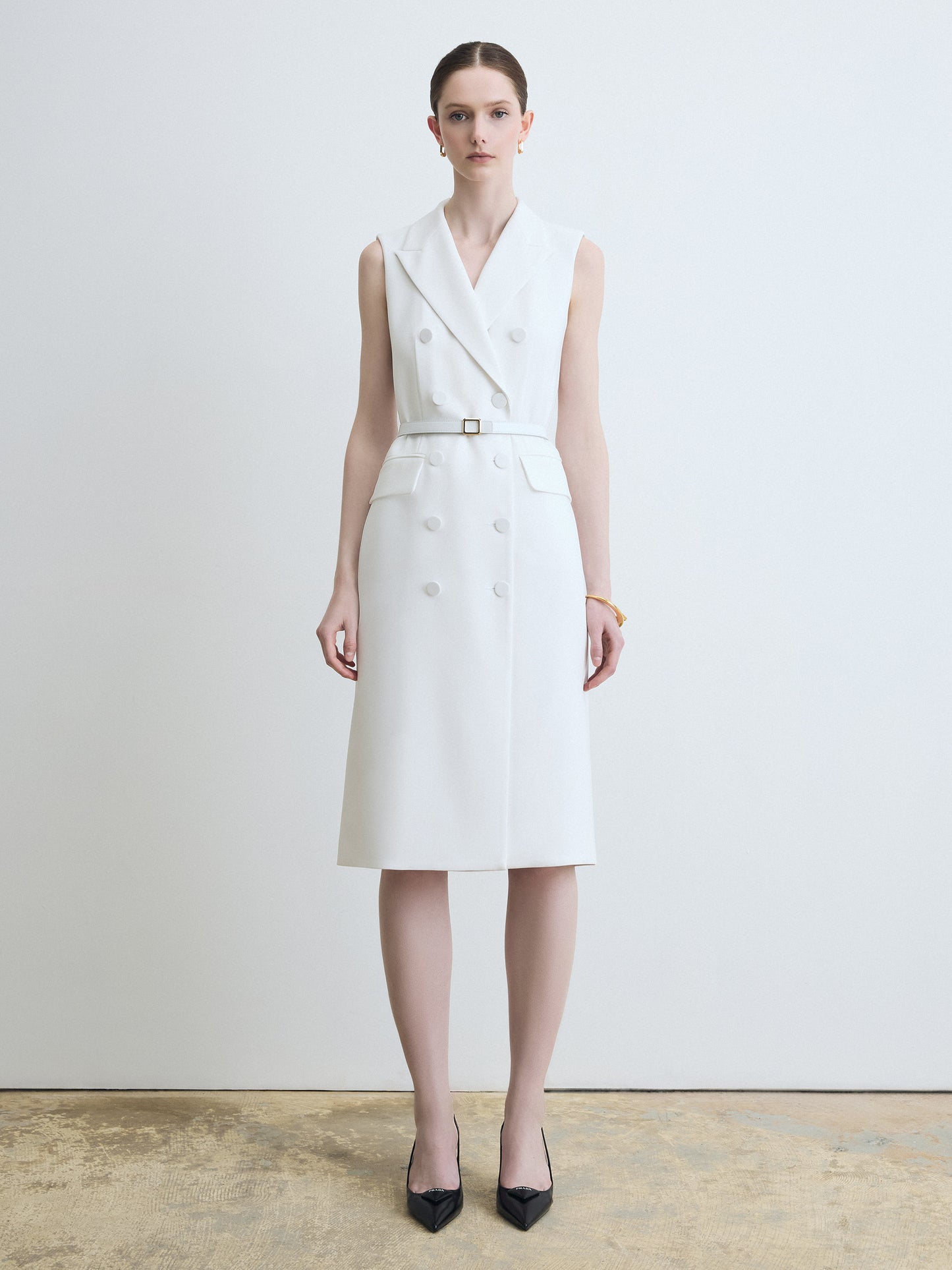 Woman wearing a white sleeveless dress with a belt against a plain background