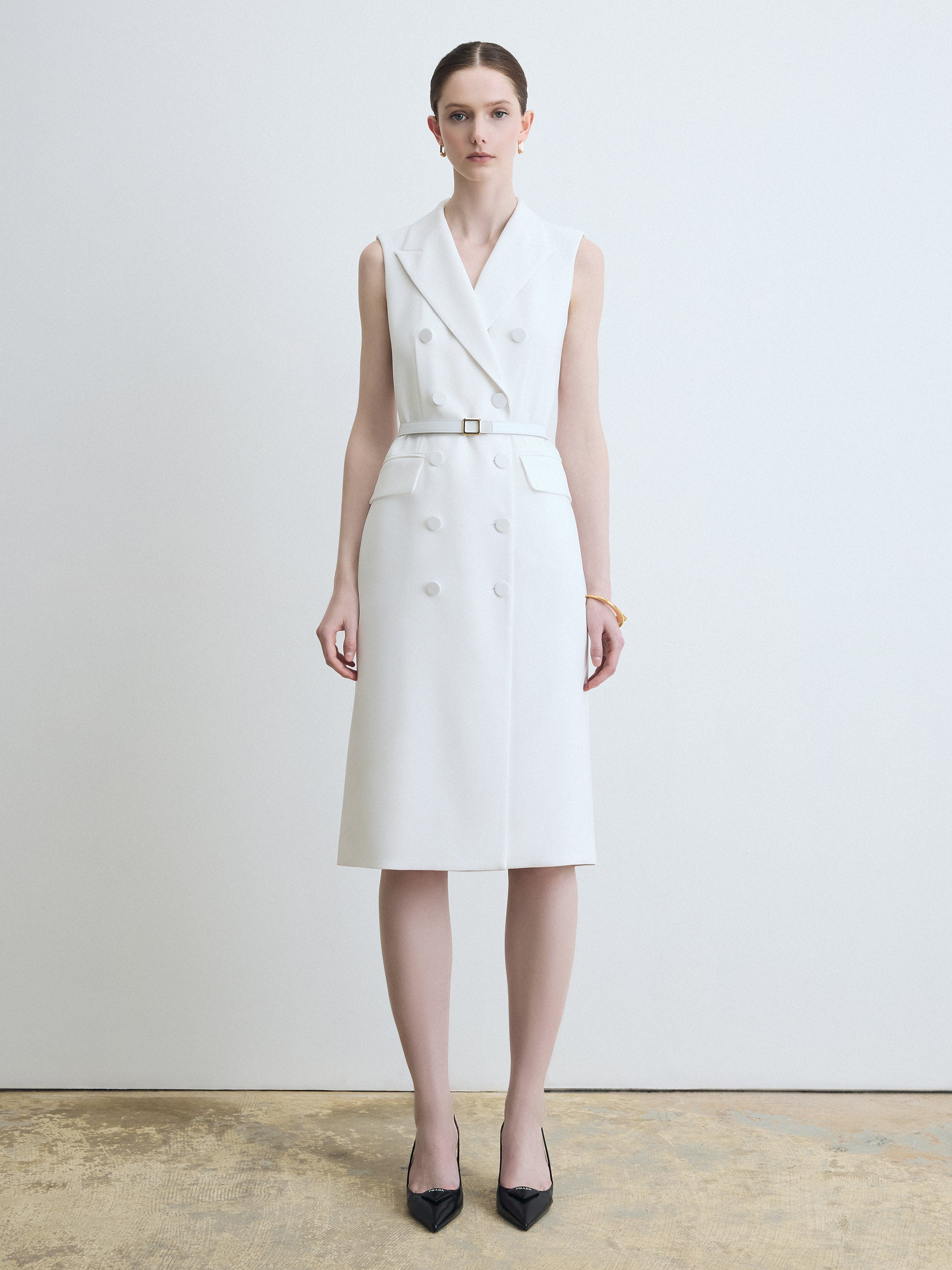 Woman wearing a white sleeveless dress with a belt against a plain background