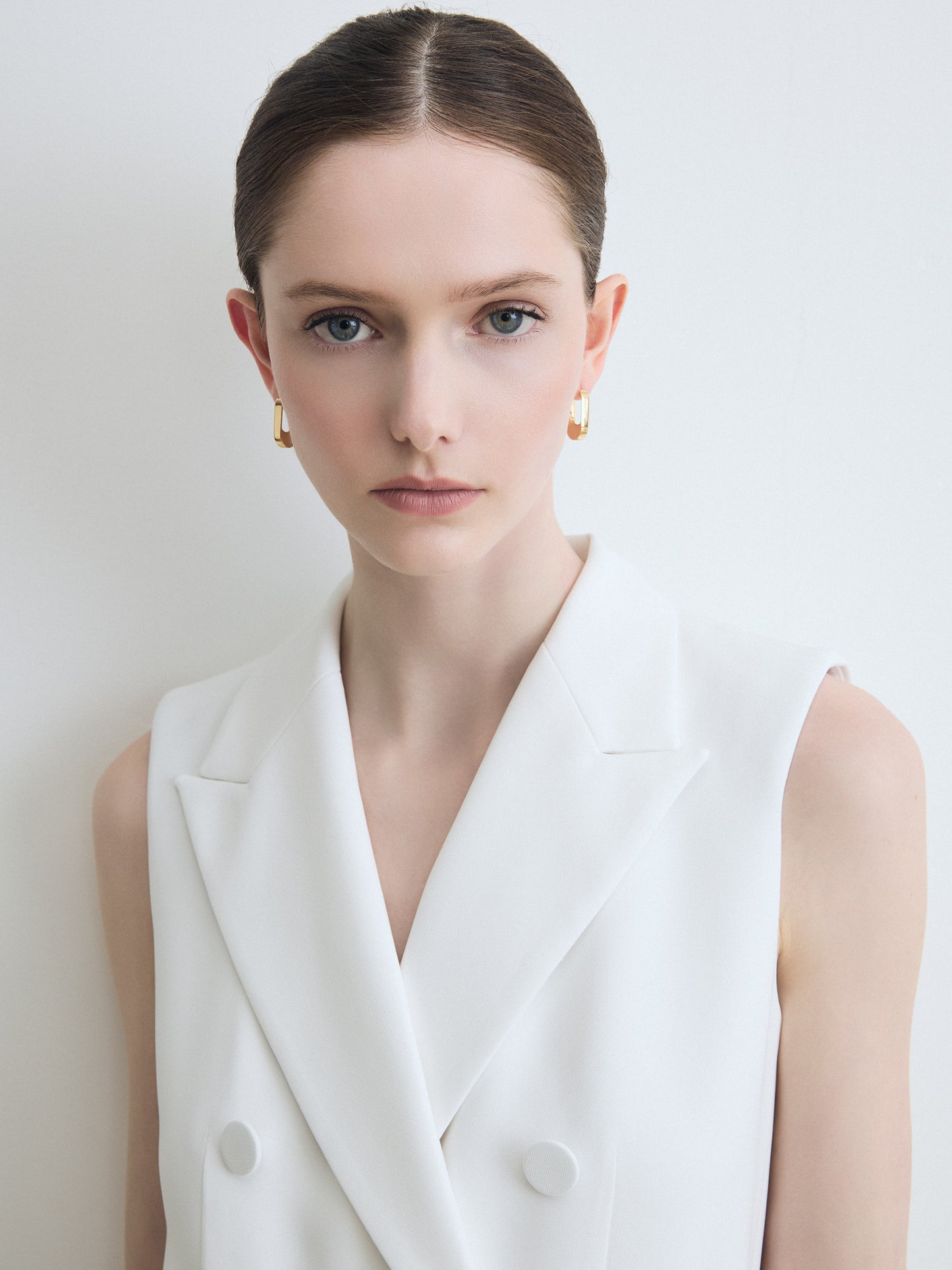 Woman wearing a white sleeveless blazer against a plain background