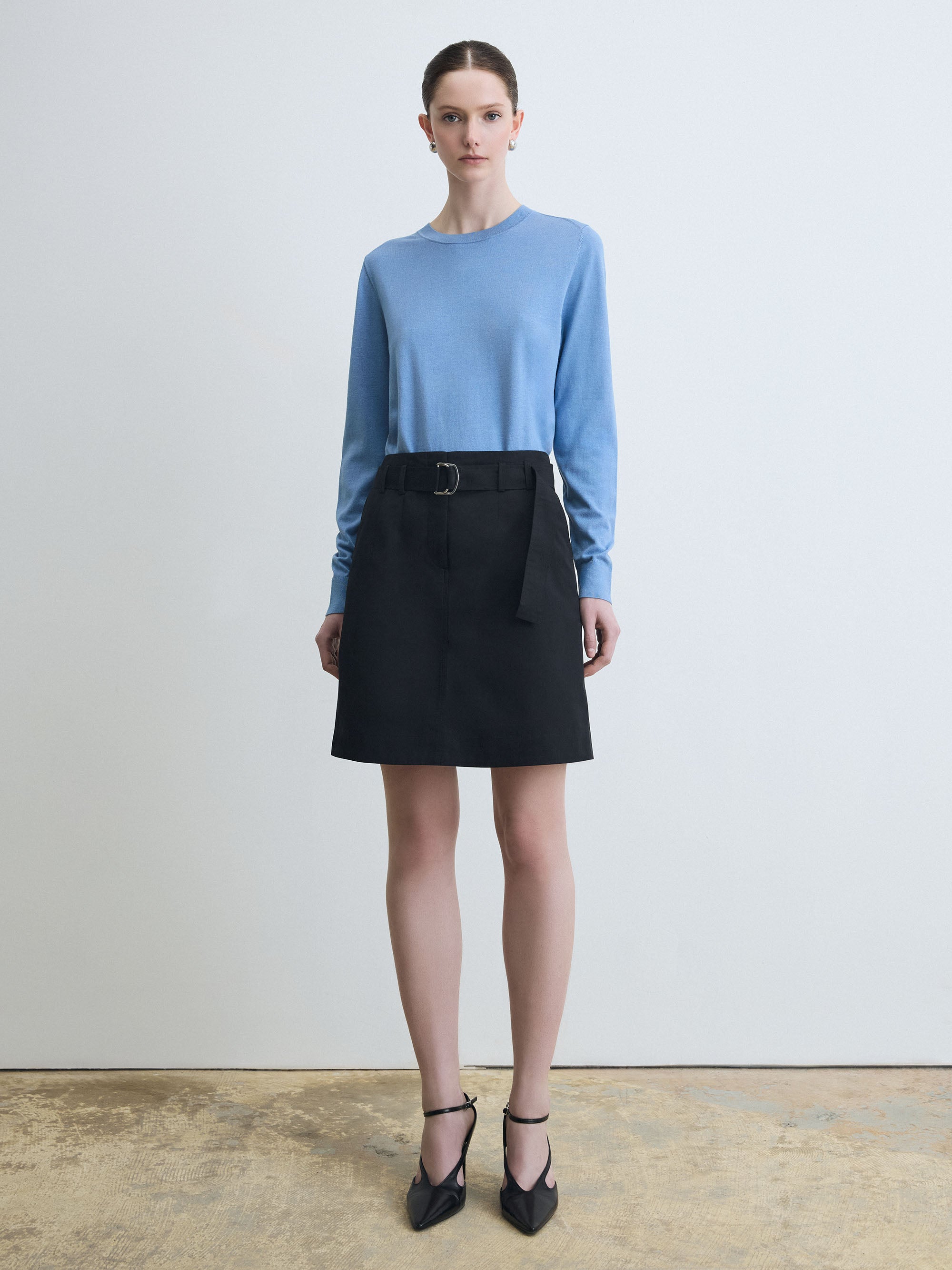 Woman wearing a blue sweater and black skirt against a white background