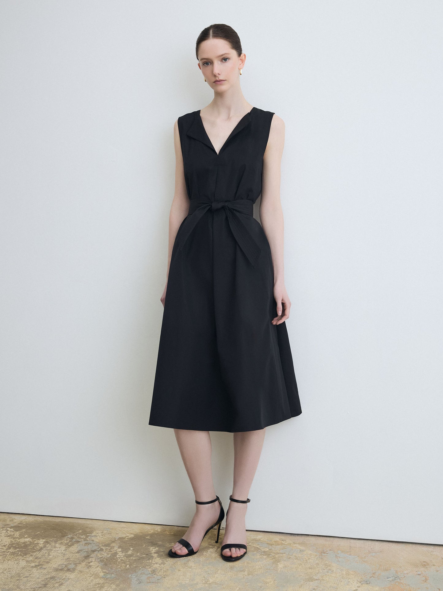 Woman wearing a black sleeveless dress against a plain background