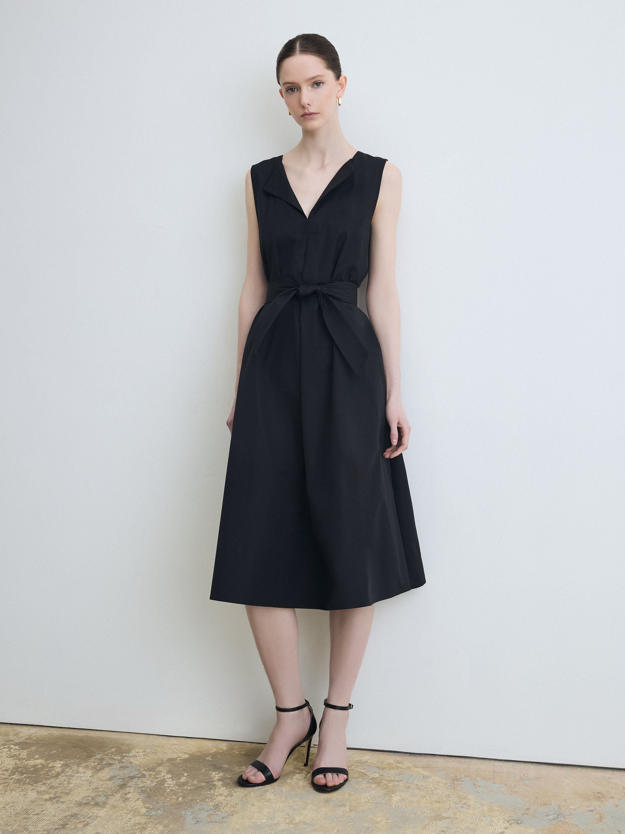 Woman wearing a black sleeveless dress against a plain background