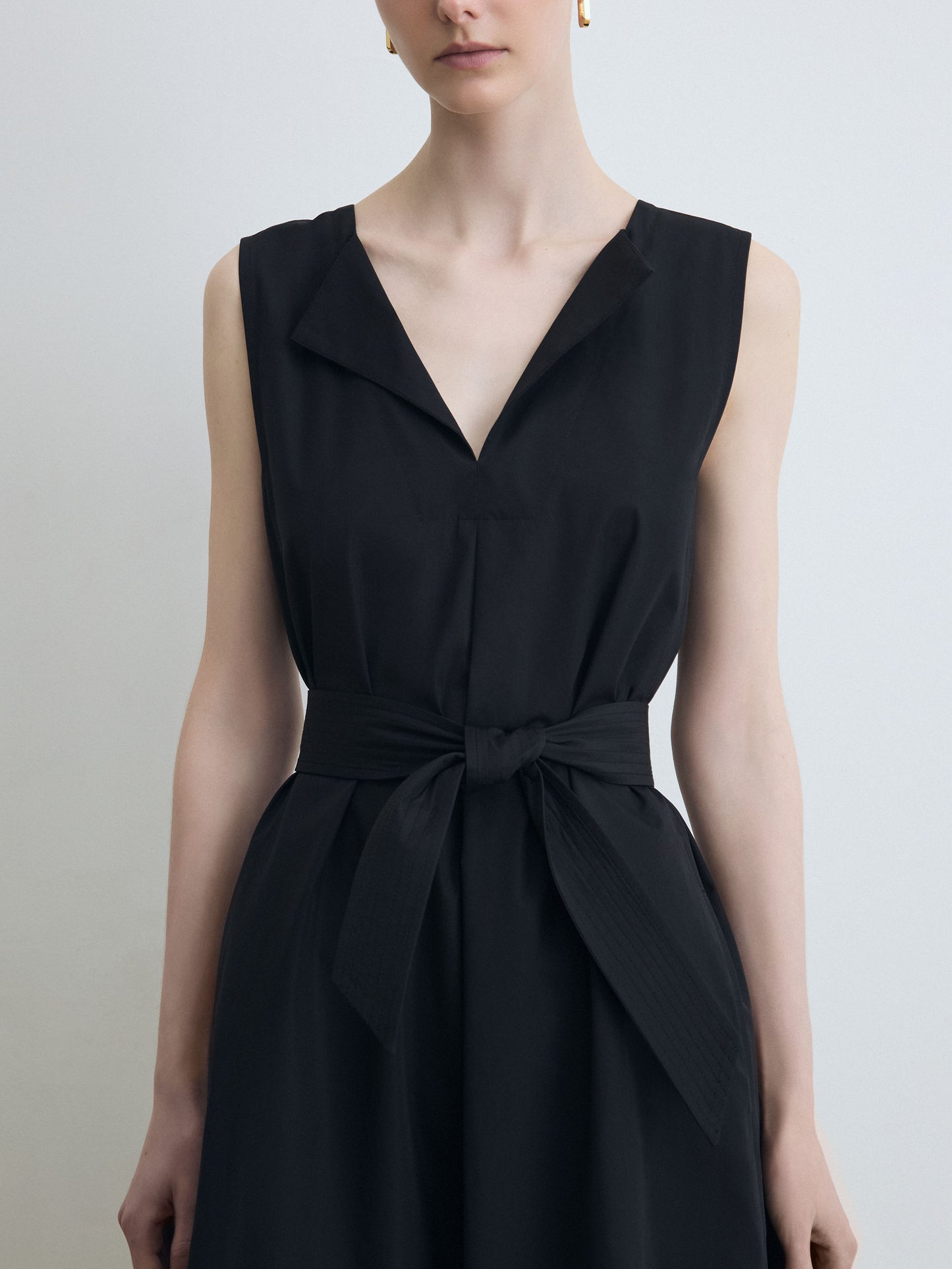 Black sleeveless dress with a tie waist on a plain background