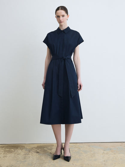 Woman wearing a navy dress with a belt against a plain background