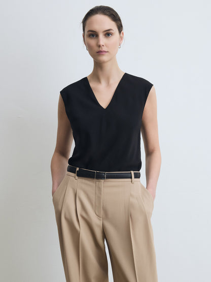 Woman wearing a black sleeveless top and beige pants against a light background