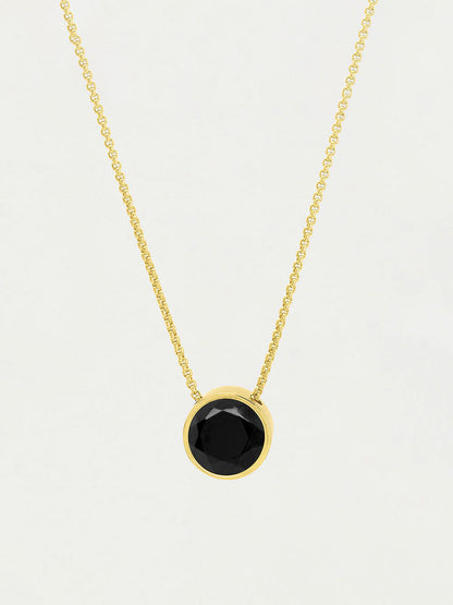 Gold necklace with a black gemstone pendant on a light gray background