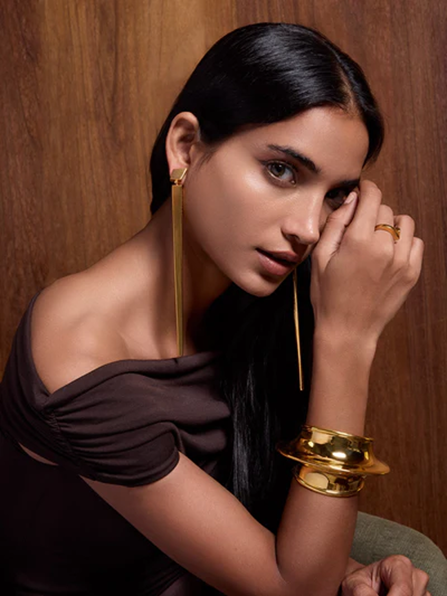 Woman wearing gold earrings and bracelet against a wooden background