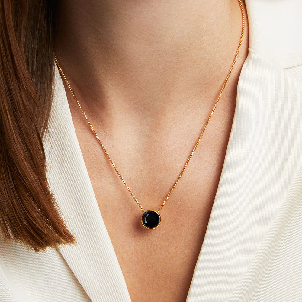 Woman wearing the Signature Knockout Pendant features a multi-faceted, brilliant-cut gemstone suspended on a fluid, adjustable box chain.