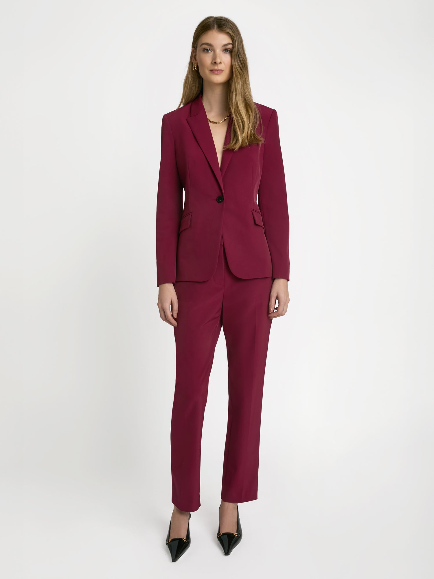 A woman modeling a mid-rise, ankle-length slim pant in a raspberry color, made from Easy Care Techno fabric.