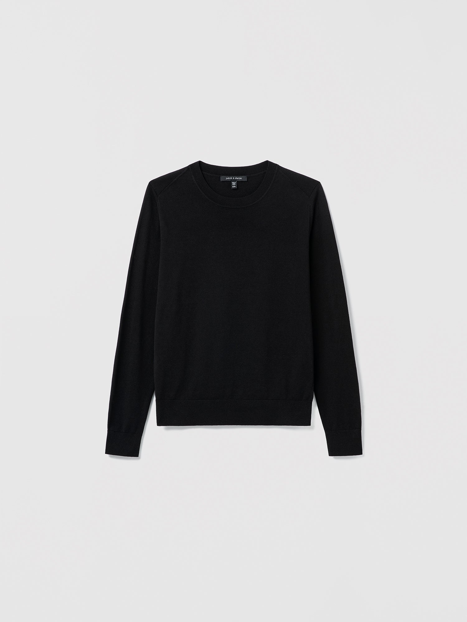 Flat‑lay of a black silk‑cotton crewneck sweater with long sleeves and refined ribbed trims.