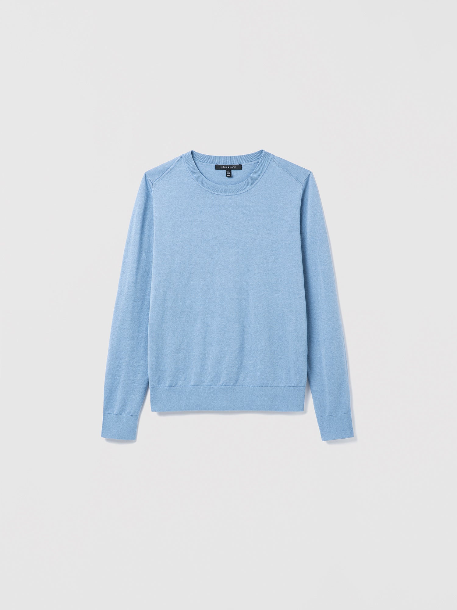 Flat‑lay of a smokey blue silk‑cotton crewneck sweater with long sleeves and refined ribbed trims.