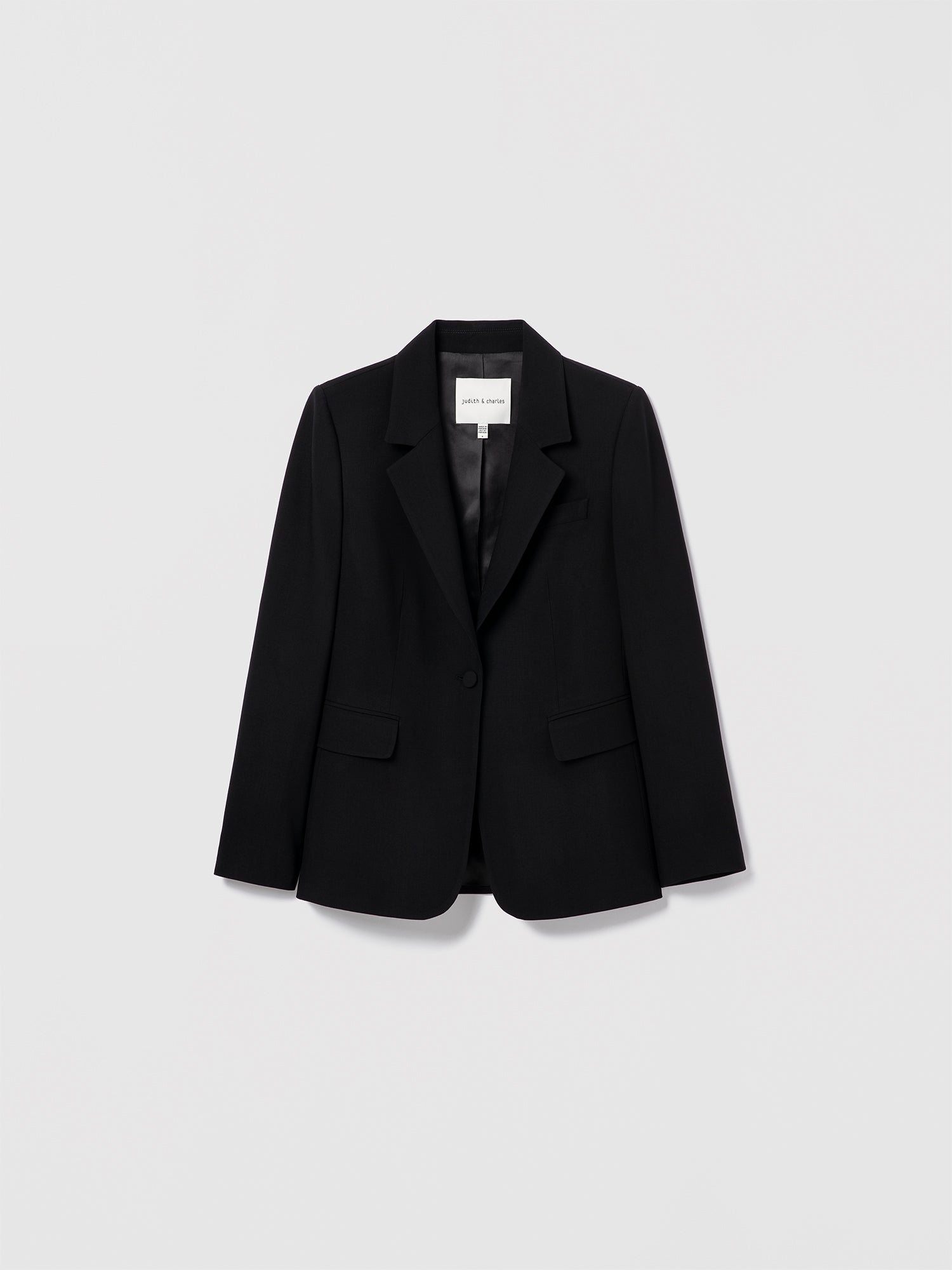 Black structured virgin wool-blend jacket by Judith & Charles, with a notch lapel, flap pockets, self-covered buttons, and a single back vent. Fully lined.